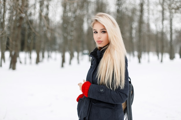 Mujer joven de moda en un elegante abrigo de moda en el parque en un día de nieve de invierno