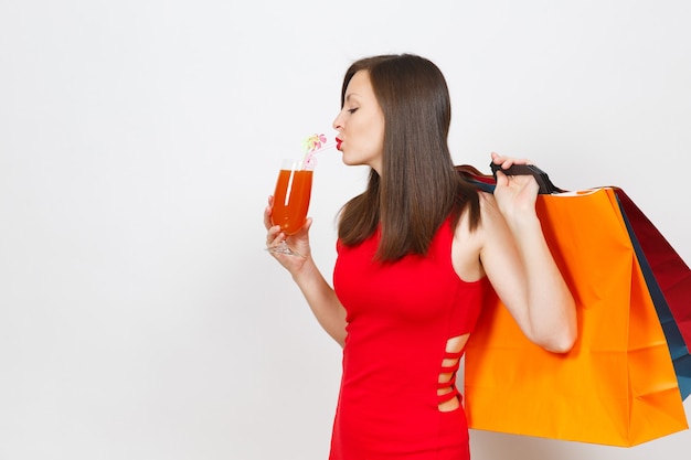 Foto mujer joven de moda glamour atractivo en vestido rojo con copa de cóctel de bebida, paquetes multicolores con compras después de ir de compras aisladas sobre fondo blanco. copie el espacio para publicidad.