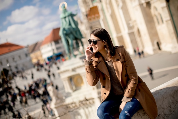 Mujer joven de moda que se sienta al aire libre y que usa el teléfono móvil