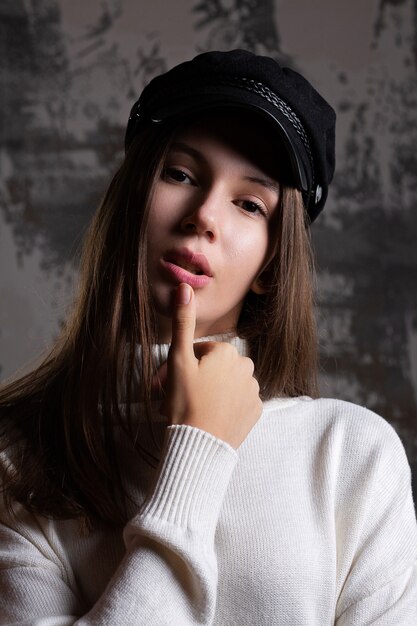 Mujer joven de moda usa gorra y suéter de punto blanco posando en el estudio con sombra en su rostro