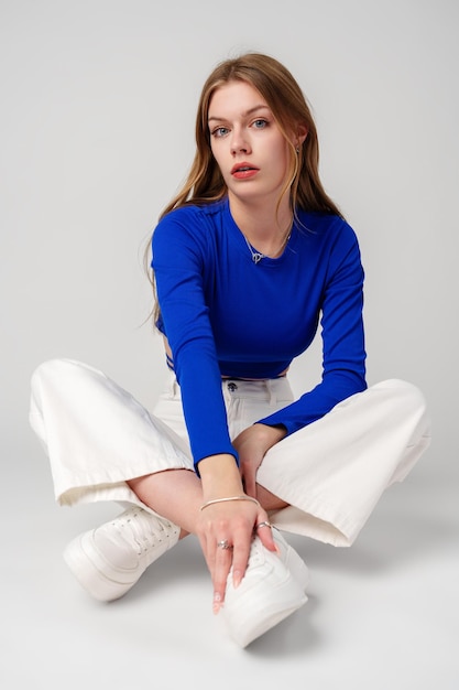 Mujer joven modelo con camiseta azul y pantalones blancos posando sobre un fondo blanco