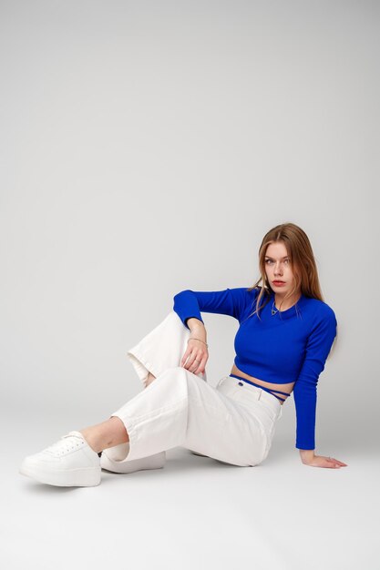 Mujer joven modelo con camiseta azul y pantalones blancos posando sobre un fondo blanco