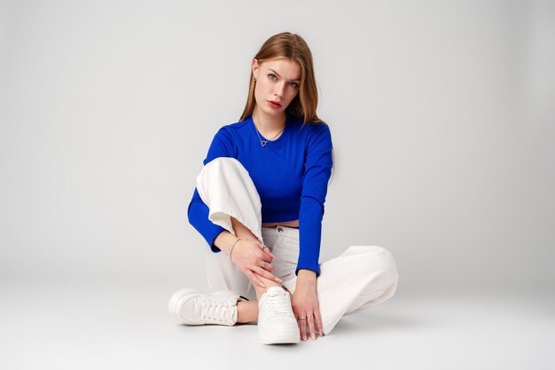 Mujer joven modelo con camiseta azul y pantalones blancos posando sobre un fondo blanco