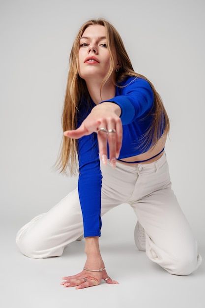 Mujer joven modelo con camiseta azul y pantalones blancos posando sobre un fondo blanco