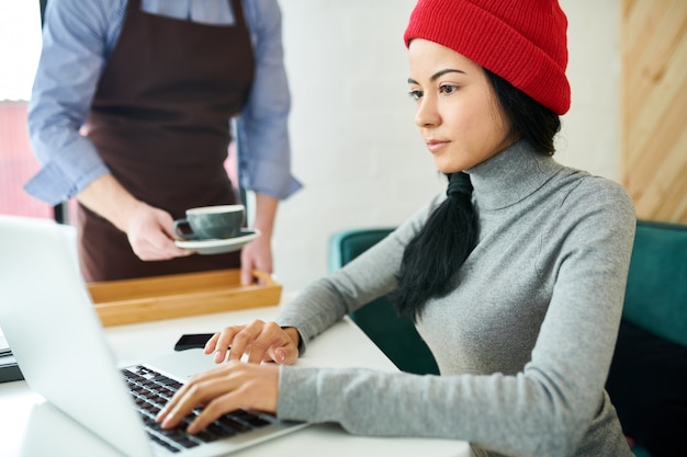 Mujer joven moderna usando laptop en café