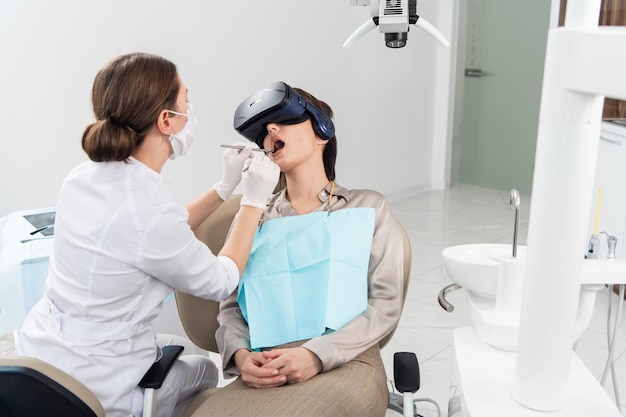 Una mujer joven en un moderno tratamiento dental, usando gafas de realidad virtual para distraerla de los desagradables procedimientos dentales.