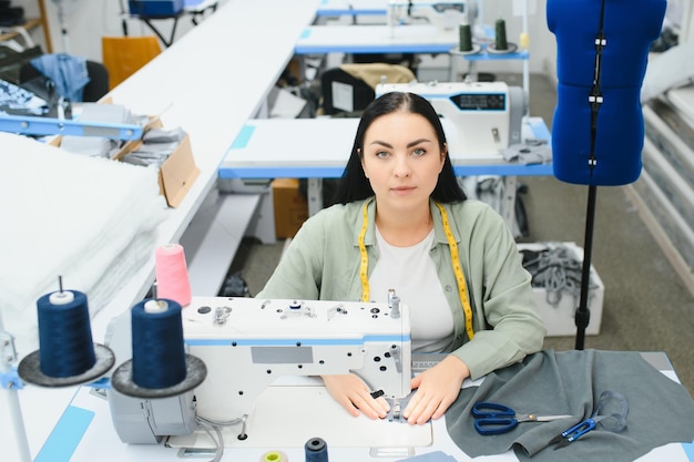 Mujer joven modista cose ropa en la mesa de trabajo Costurera sonriente y su mano de cerca en el taller