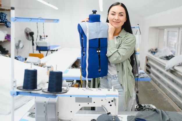 Foto mujer joven modista cose ropa en la mesa de trabajo costurera sonriente y su mano de cerca en el taller