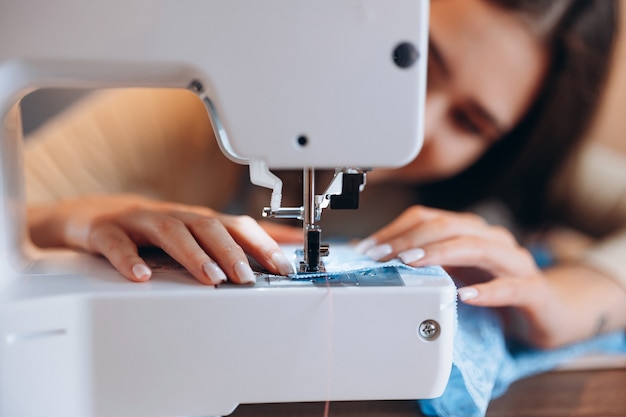 Mujer joven modista cose ropa en primer plano de la máquina de coser