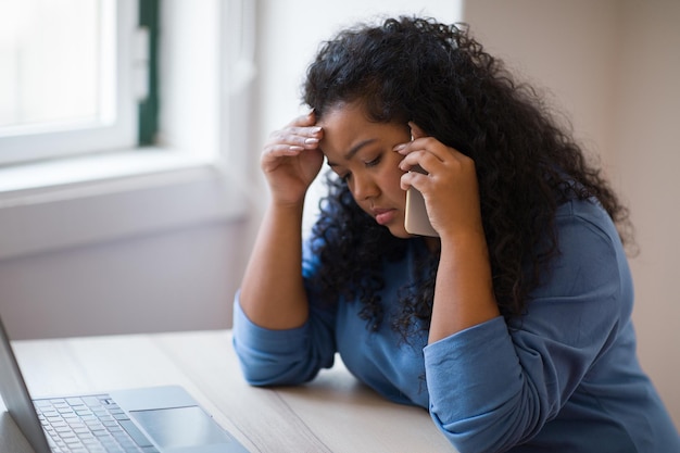 Mujer joven molesta sentada en el escritorio trabajando en línea en la computadora portátil