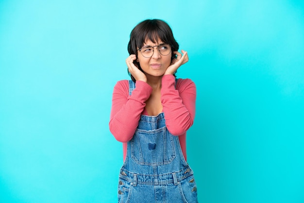 Mujer joven con un mono de fondo aislado frustrado y cubriendo las orejas