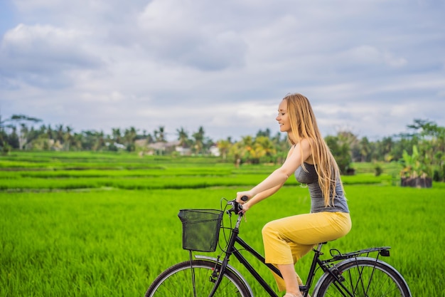 Una mujer joven monta una bicicleta en un campo de arroz en Ubud Bali Bali Travel Concept