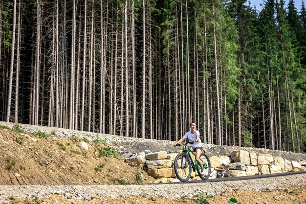 Una mujer joven monta una bicicleta en una zona montañosa del bosque.