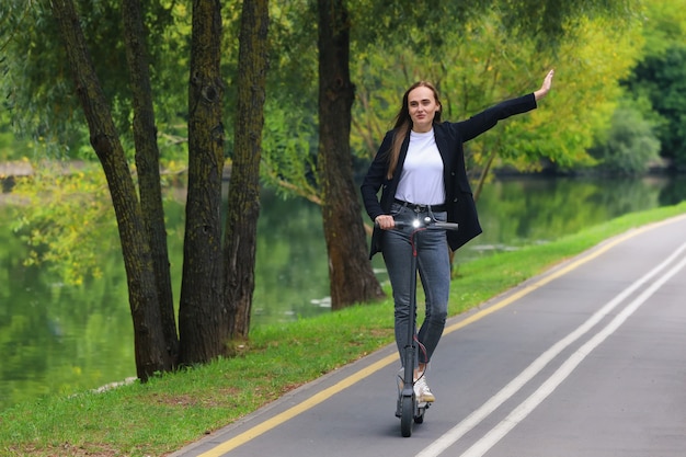 Una mujer joven monta un scooter eléctrico en un carril bici en el parque