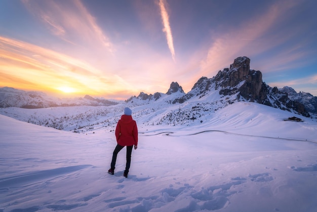 Mujer joven en montañas nevadas al atardecer en invierno Paisaje con hermosa chica delgada en la colina contra rocas cubiertas de nieve y cielo colorido con nubes en la noche Viajes en Dolomitas Turismo