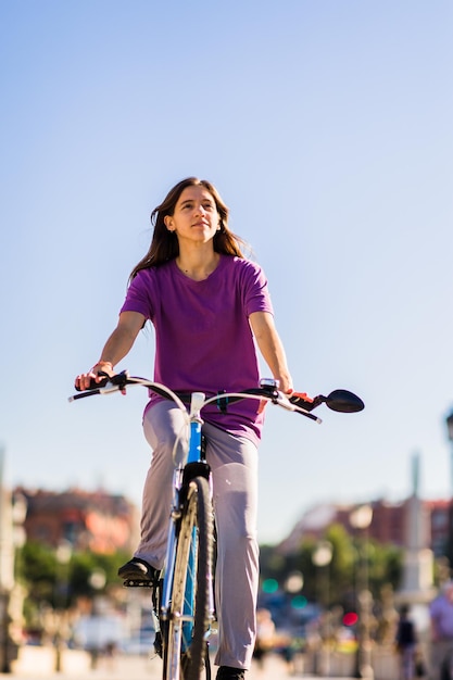 Foto mujer joven montando bicicleta en la calle contra un cielo despejado