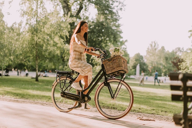 Mujer joven montando bicicleta eléctrica con flores en la cesta