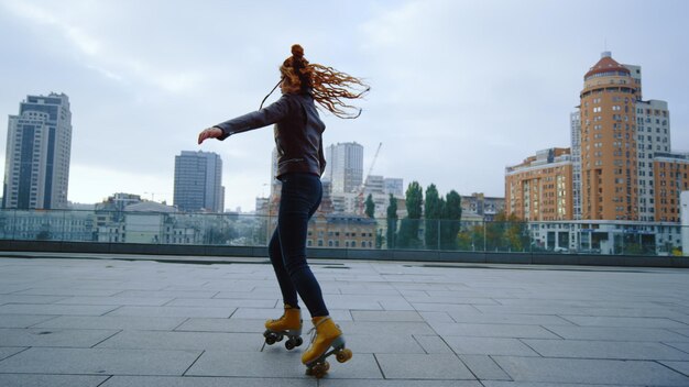Foto mujer joven montando en patines sobre fondo urbano chica hipster deportiva realizando elementos de patinaje al aire libre patinador activo bailando fuera del concepto de deportes callejeros