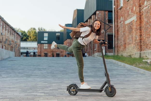 Mujer joven montando scooter eléctrico en la calle urbana de la ciudad