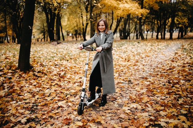 Mujer joven montando un scooter eléctrico en un parque de la ciudad en otoño