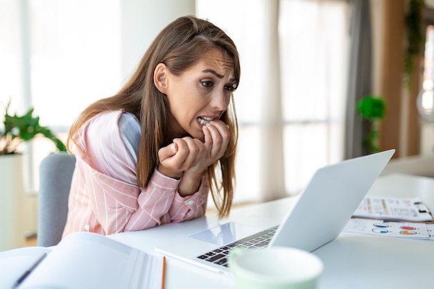 Mujer joven mordiéndose las uñas mientras trabaja en una computadora portátil en casa Mujer ansiosa que trabaja en la oficina mordiéndose los dedos y las uñas