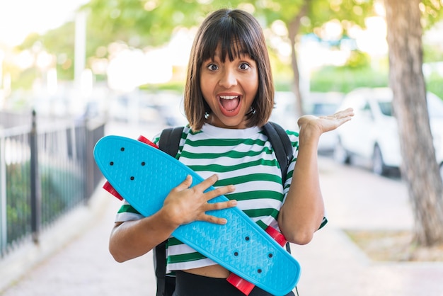 Mujer joven morena al aire libre con un patín y haciendo gesto de sorpresa