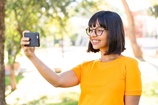 Mujer joven morena al aire libre mediante teléfono móvil y haciendo un selfie