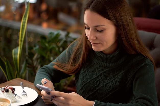 Mujer joven morena en café con portátil se comunica por teléfono inteligente
