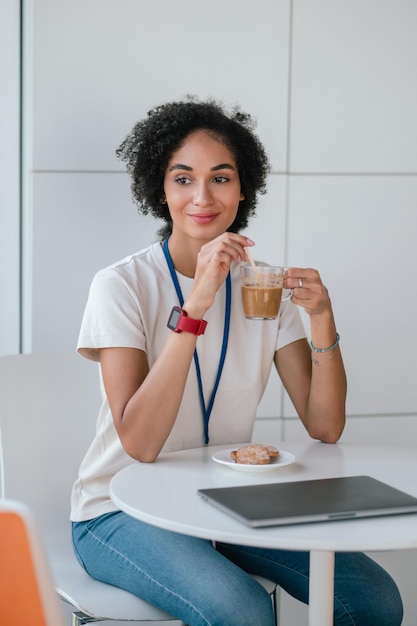 Mujer joven morena en la cantina de la oficina tomando un café