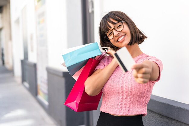 Foto mujer joven morena en la ciudad con bolsas de compras y una tarjeta de crédito