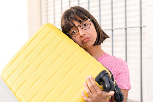 Foto mujer joven morena en la ciudad de vacaciones con maleta de viaje e infeliz