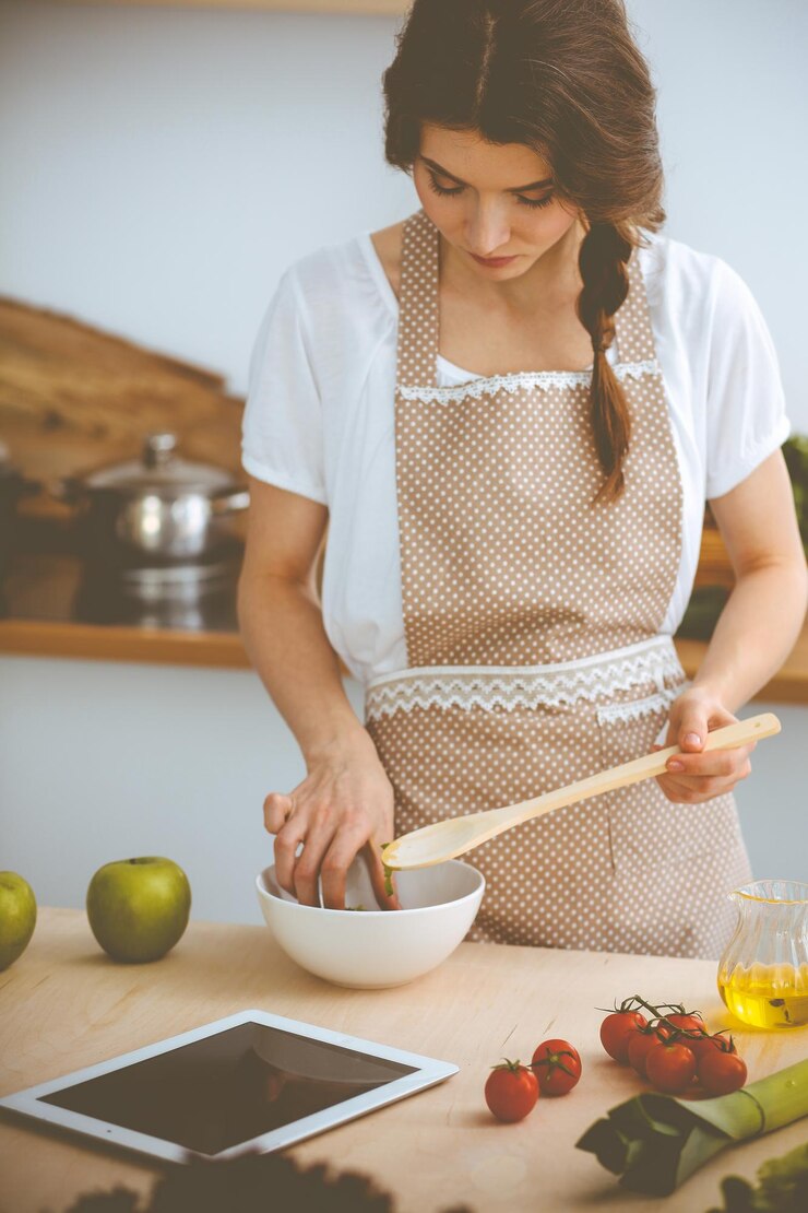 Foto mujer joven morena cocinando en la cocina. ama de casa con cuchara de madera en la mano. concepto de comida y salud.