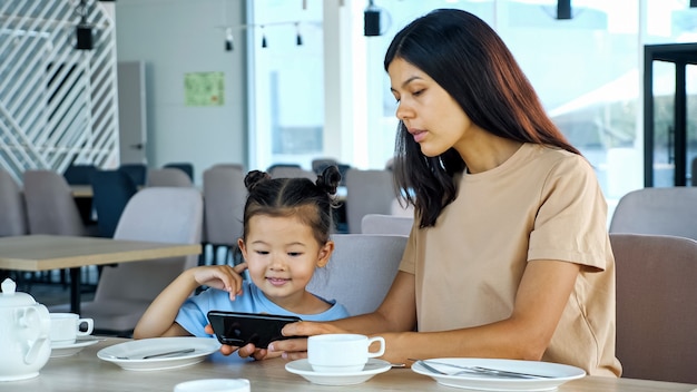 Mujer joven morena y niño pequeño ver video en gadget