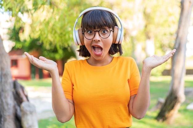 Mujer joven morena en el parque sorprendido y escuchando música