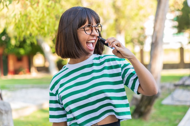 Mujer joven morena en el parque mediante teléfono móvil y cantando