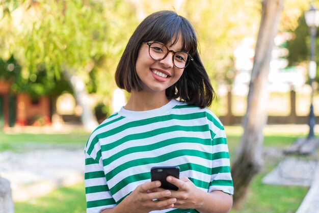 Mujer joven morena en el parque mediante teléfono móvil