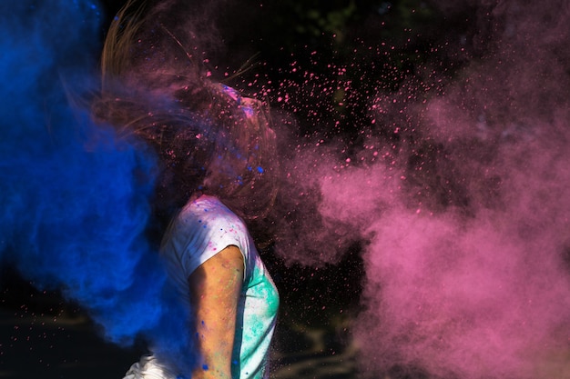 Mujer joven morena con el pelo en movimiento divirtiéndose con coloridos polvos Holi