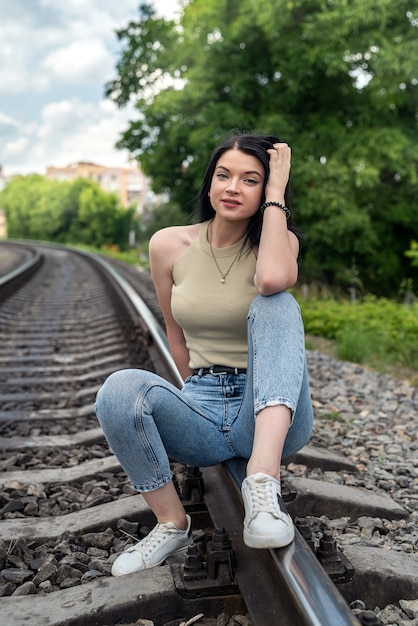 Mujer joven morena de pie sobre las vías del tren, viaje de verano