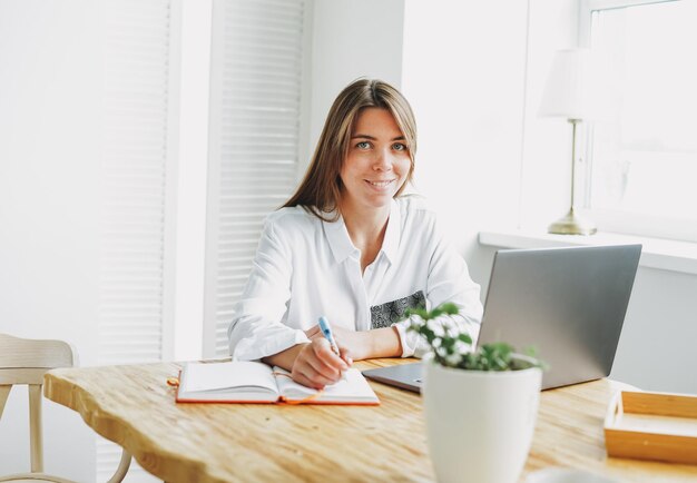 Foto mujer joven morena que trabaja como freelancer con ropa casual y portátil en casa.