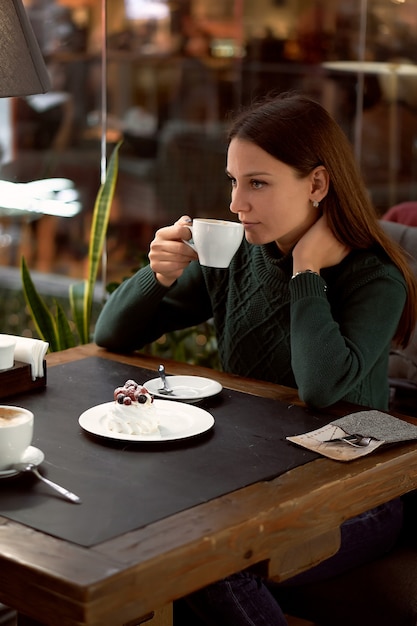 Mujer joven morena tomando café en un café y comiendo postre