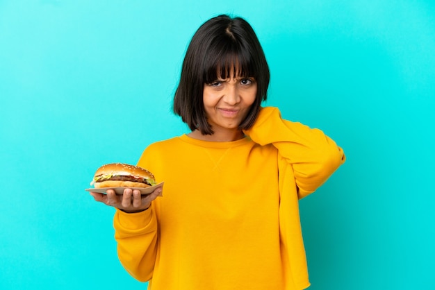 Mujer joven morenita sosteniendo una hamburguesa sobre antecedentes aislados teniendo dudas