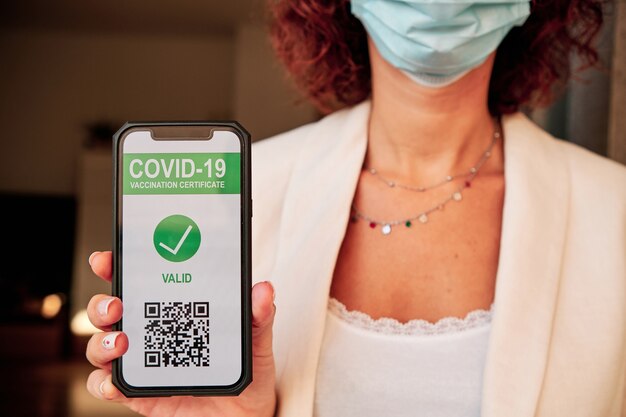 Foto mujer joven mostrando pasaporte sanitario de vacunación en smartphone con código qr para turismo - covid-19