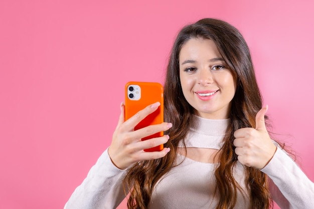 Mujer joven mostrando el pulgar hacia arriba en como o la aprobación de un nuevo bien sosteniendo un teléfono inteligente de pie en el