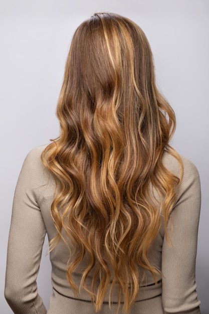 Mujer joven mostrando su hermoso cabello después de teñir y peinar en un salón profesional