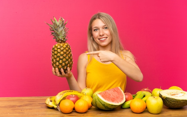 Mujer joven con muchas frutas sosteniendo una piña