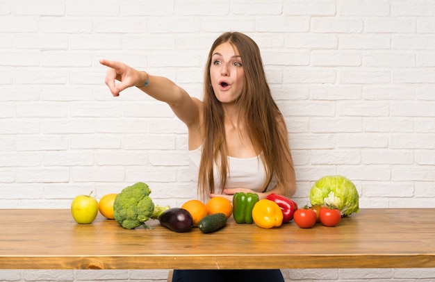 Mujer joven con muchas verduras apuntando lejos