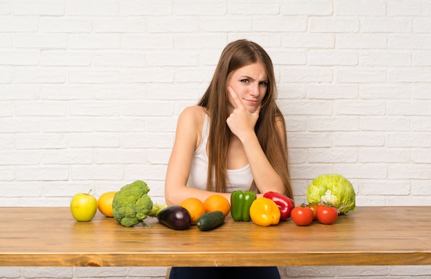 Mujer joven con muchas verduras de pie y pensando una idea