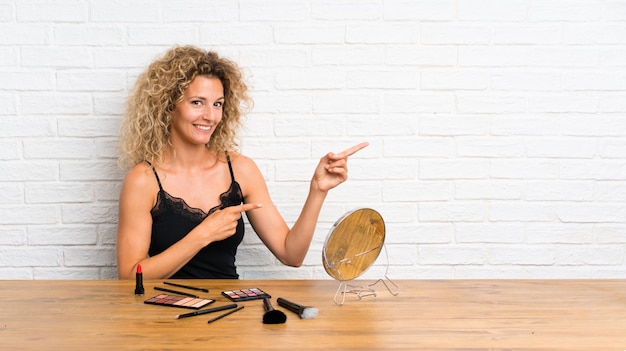 Mujer joven con mucho pincel de maquillaje en una mesa apuntando con el dedo hacia un lado