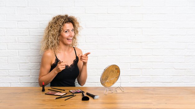 Mujer joven con mucho pincel de maquillaje en una mesa te señala con el dedo