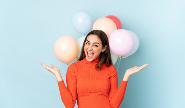 Mujer joven con muchos globos aislados en azul